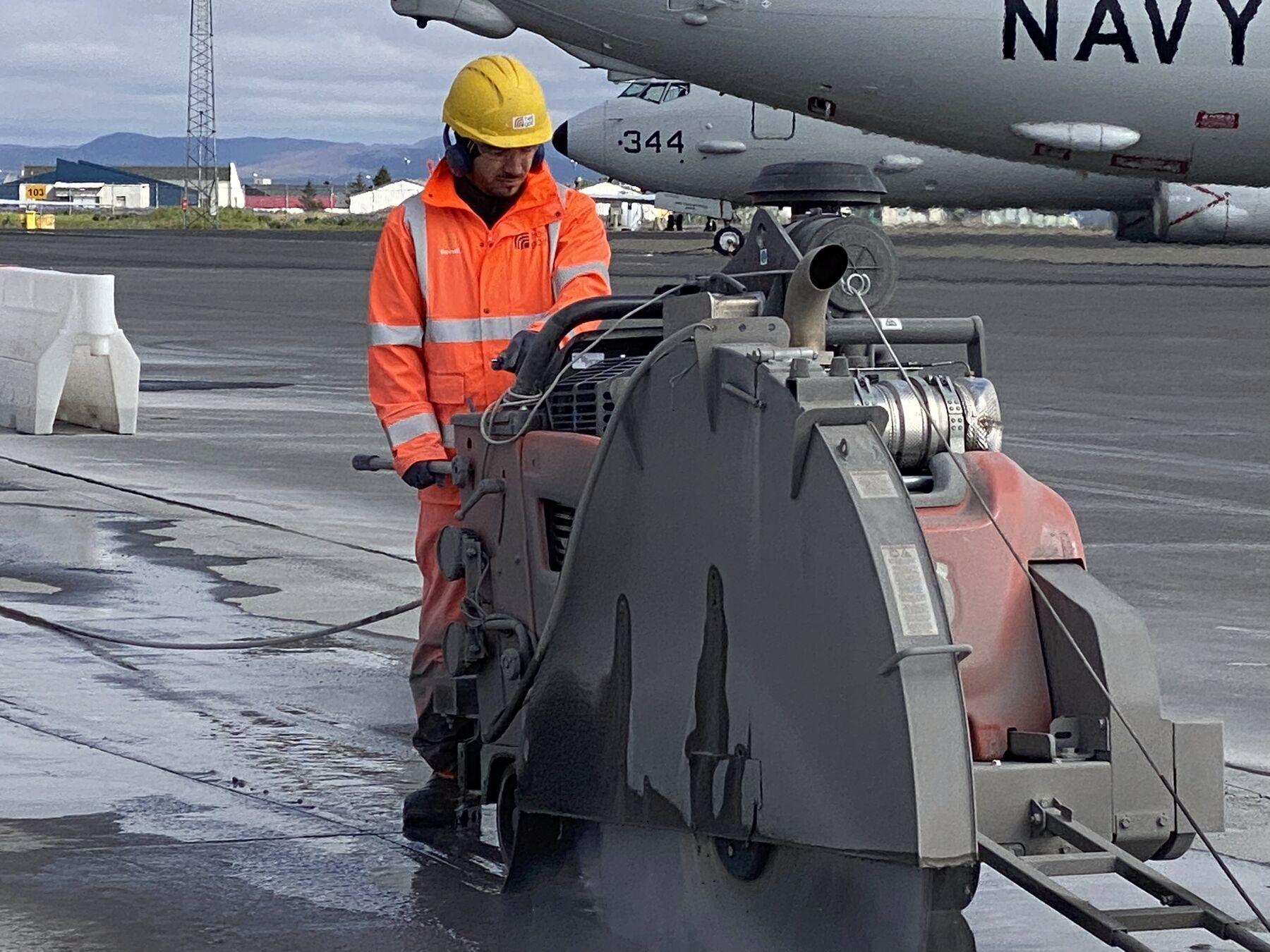 Starfsmaður sagar steypta plötu með stórri gólfsög á flugvelli