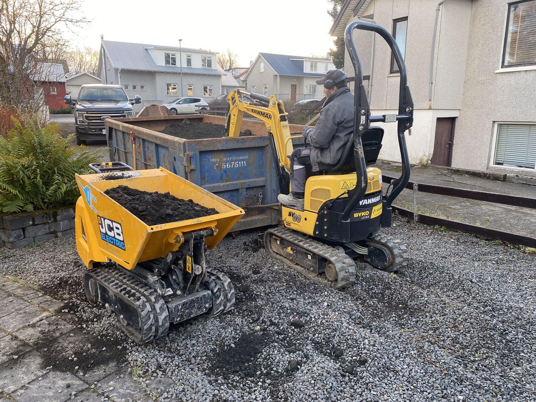 Beltavagn og smágrafa fylla gám af efni fyrir utan hús